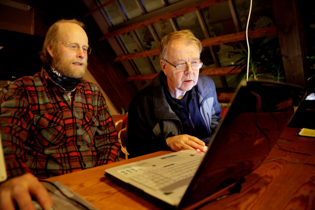 To personer som hjelper hverandre med slektsforskning foran en PC.